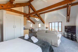 Ein Schlafzimmer mit Bett, einer Couch, einem Fernseher und Blick aufs Meer.