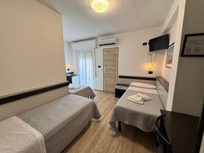 Habitación de hotel con dos camas individuales, un escritorio, una silla, un televisor fijado a la pared y un aire acondicionado.