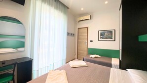 Hotellihuone, jossa on kaksi sänkyä, työpöytä, tuoli, ilmastointilaite ja ovi.
