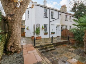 A white building with a stone pathway leading to the entrance, surrounded by greenery and a large tree. - 1A Coastguard Cottages, Rye Harbour (Rye)