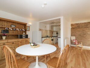 Un coin repas avec une table ronde et des chaises en bois, une cuisine dotée d’un plan de travail en bois et d’appareils électroménagers, et un mur en briques.
