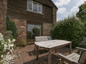 A rustic wooden house with a patio, a table, and benches.