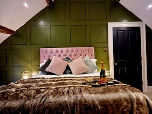 A bedroom with a tufted headboard, a fur throw, a bottle of champagne, and a tray with snacks.