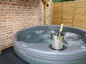 A hot tub with a bottle of champagne, surrounded by a brick wall and wooden fence. - Tawny Barn, Woodhall Spa (Lincoln)