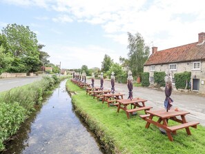 Une rangée de tables de pique-nique longe un étroit canal, avec des bâtiments en pierre d’un côté.