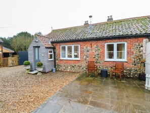 A brick house with a tiled roof, a stone patio, and a small garden area with two wooden chairs.
