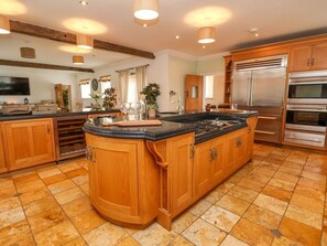 A kitchen with wooden cabinets, a large island, stainless steel appliances, and a tiled floor. - The Wing, Bangor-On-Dee, Wales (Wrexham)