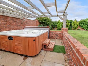 A hot tub under a wooden pergola, surrounded by a brick wall and a grassy lawn. - The Wing, Bangor-On-Dee, Wales (Wrexham)