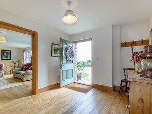 Ein Zimmer mit Holzboden, einer Tür, die nach draußen führt, einer Küchenzeile mit Herd und einem Esstisch mit Stühlen.