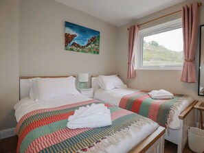 Ein Schlafzimmer mit zwei Betten, einem Bild an der Wand, einem Fenster mit Vorhängen und einem Nachttisch mit Lampe.
