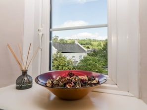 A window with a view of a house, a bowl of dried flowers, and a reed diffuser. - The Retreat, Harbertonford (Totnes)