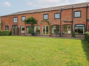 A brick building with multiple windows and doors, a grassy lawn, and outdoor seating.