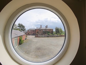 A view through a circular window of a building with a paved courtyard and a brick structure.