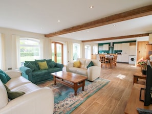 A spacious living area with a sofa, coffee table, and a dining table with chairs. A kitchen is visible in the background.