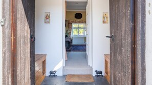 A hallway leading to a room with a radiator, a window, and a door with a rustic appearance. - Field Head House, Hawkshead (Ulverston)