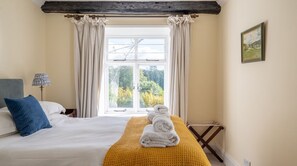 A bedroom with a bed, a window with curtains, a lamp, and a painting on the wall. - Field Head House, Hawkshead (Ulverston)