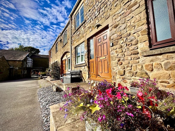 A stone building with a wooden door, a window, and a flower bed in the foreground.