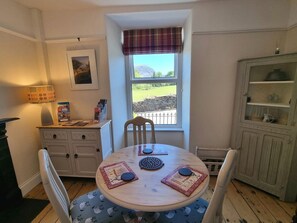 A dining area with a round table, chairs, a window with a view, a cabinet with glass doors, and a lamp.