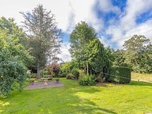 A garden with a wooden bench, a stone planter, and various trees.