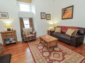 A cozy living room with a wooden floor, a plaid armchair, a brown leather sofa, a coffee table, and a patterned rug.