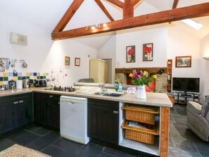 A kitchen with dark cabinets, a dishwasher, a sink, and a stove. There is a dining area with a table and chairs, and a television in the background.
