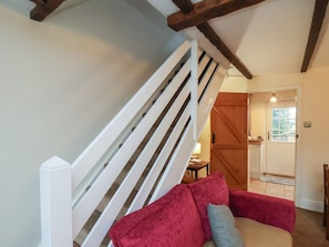 A staircase with white railings, a red sofa, and a wooden door in the background. - 4 Lilac Cottages, Ainthorpe (Whitby)