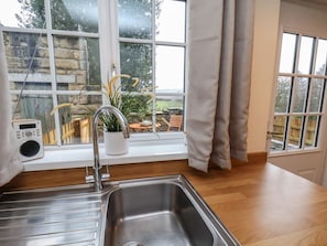 A kitchen with a stainless steel sink, a radio, and a window with curtains. - 4 Lilac Cottages, Ainthorpe (Whitby)