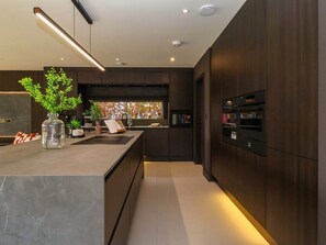 A modern kitchen with dark wood cabinets, a marble countertop, and built-in appliances. - Woldside, Bishop Wilton (York)