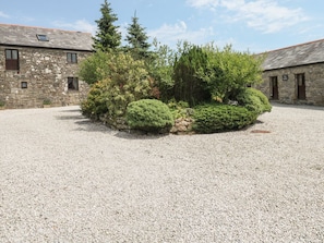 A stone building with a gravel courtyard, surrounded by dense shrubbery and trees.