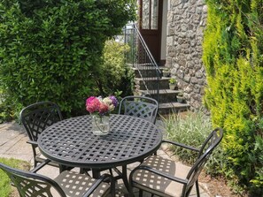 A round metal table with chairs, a vase with flowers, and a stone wall with a staircase. - The Hayloft, St Neot (Liskeard)