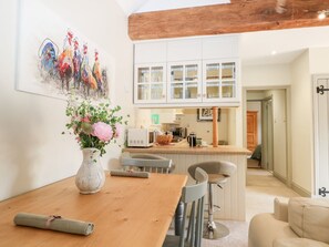 A dining area with a wooden table, a vase of flowers, and a kitchen in the background. - Hungers Cottage, Petworth. (Petworth)
