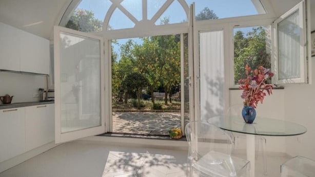A modern kitchen with white cabinets, a glass door leading to a garden, and a clear glass table with chairs. - Dimora Filangieri (Massa Lubrense)