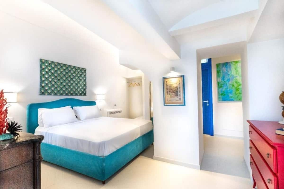 A bedroom with a bed, a nightstand, a red dresser, and a blue door.