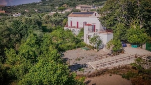 A coastal building with a red door, surrounded by greenery and a sandy area. - Dimora Filangieri (Massa Lubrense)