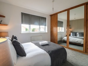 A bedroom with a bed, a bedside table, a lamp, a window with blinds, and a sliding door leading to another room.