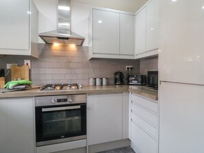 A modern kitchen with white cabinetry, a built-in oven, a gas stove, and a coffee maker.