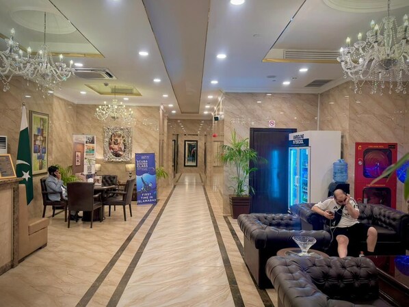 A hotel lobby with chandeliers, a reception desk, a seating area, and a water dispenser.