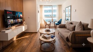 Uma sala de estar moderna com uma TV de tela plana, um sofá, uma mesa de centro e uma área de jantar com mesa e cadeiras.