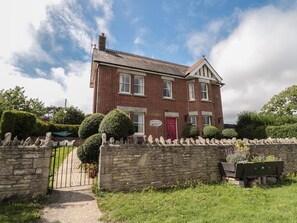A two-story brick house with a red door, stone wall, and a paved driveway leading to a gate. - The Farmhouse, Swanage, Dorset (Swanage)