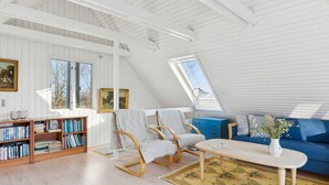 A spacious loft with a high ceiling, wooden bookshelves, a blue sofa, and a dining table. - 4 Star Holiday Home in Humble (Sydlangeland)