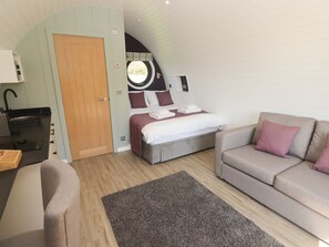 Una habitación compacta con cama, sofá, un escritorio pequeño y un ventanal circular.