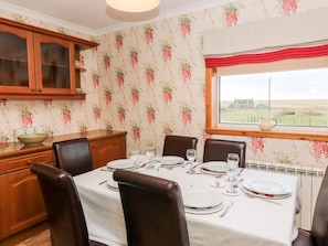 Une salle à manger avec une table dressée pour quatre personnes, des meubles en bois et une fenêtre donnant sur la campagne.