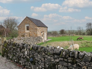 Un bâtiment en pierre doté d’un toit en pente, entouré d’un mur de pierre et d’un champ verdoyant où paissent des moutons.