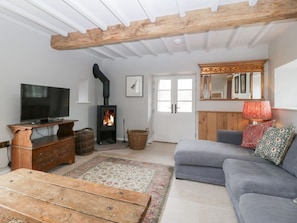 A living room with a television, fireplace, sofa, and wooden ceiling beams.