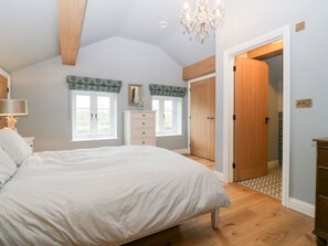 Ein Schlafzimmer mit einem großen Bett, einem Schminktisch, einem Fenster mit Vorhängen, einer Chandelieber und einer Holztür.