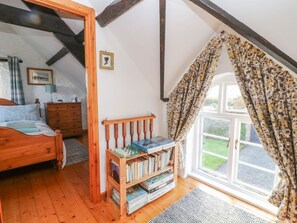 A bedroom with a wooden bed, a bookshelf, a window with curtains, and a door leading to another room.