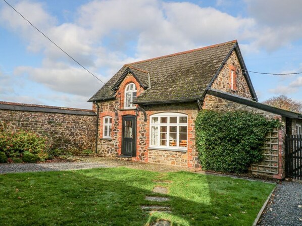 A stone house with a sloped roof, a front door, and a large window.