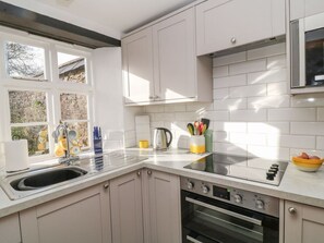 A modern kitchen with a sink, stove, oven, and window overlooking a stone wall.