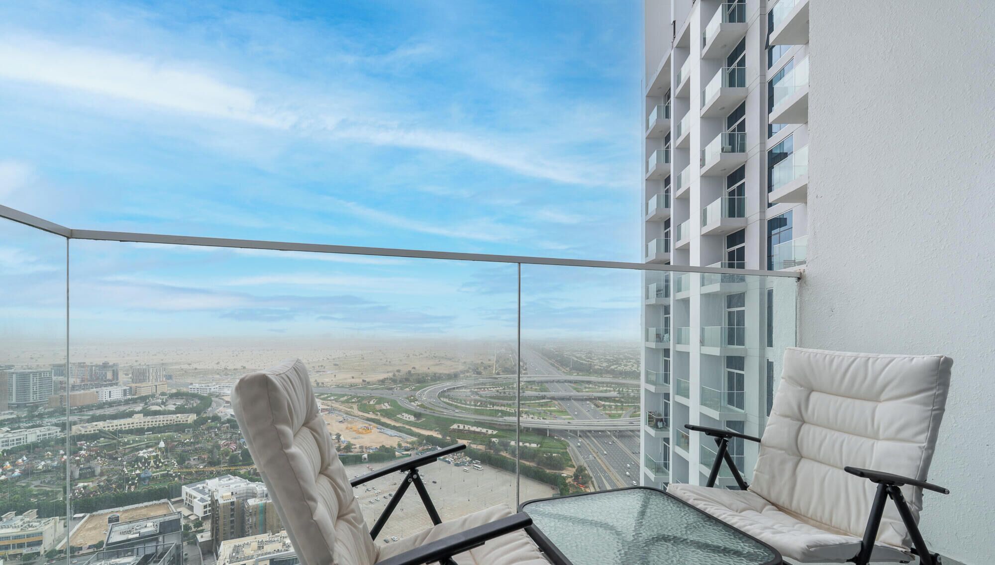 A balcony with a glass barrier, a white cushioned chair, and a table.