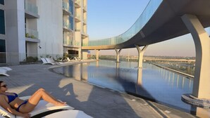 Un espace aménagé au bord de la piscine, avec des chaises longues et un pont de verre offrant une vue sur une étendue d’eau.